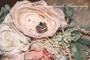 Wedding rings nestled inside a blush pink rose with delicate greenery and floral accents.