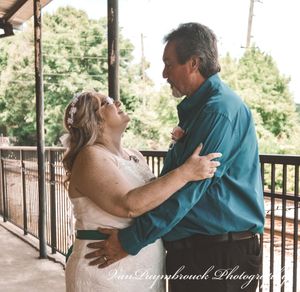 A couple shares an intimate dance moment on an outdoor wooden deck surrounded by trees.
