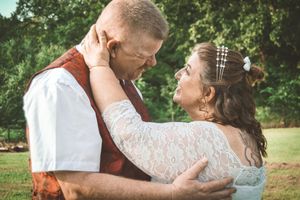 A romantic outdoor wedding moment with the couple embracing in a garden setting, wearing rustic and lace attire.