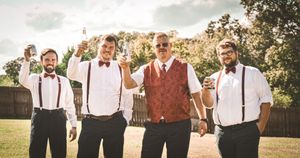 Wedding party members in burgundy and navy attire pose together outdoors in a sunny garden setting.