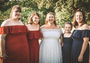 Wedding party wearing coordinated burgundy and navy outfits stands together in a natural outdoor setting.