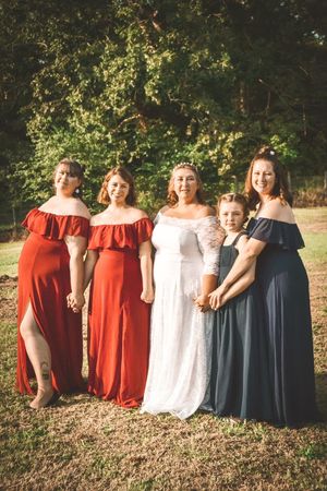 A group wearing coordinated formal dresses in red, white and navy blue poses together outdoors in a natural setting.