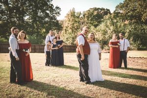 Wedding party members in red and black attire gathered outdoors during a sunset ceremony.