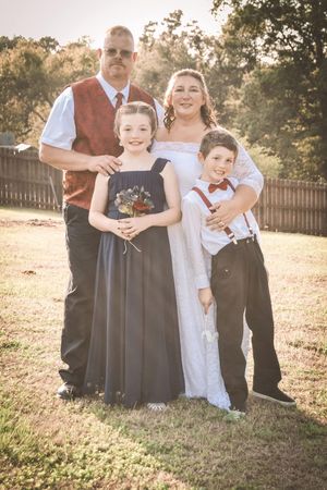 Wedding party poses together in a sunlit outdoor setting with formal attire.