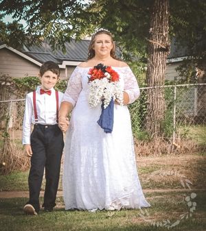 A wedding couple poses outdoors with a small child in formal attire near trees.