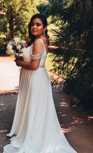 A flowing white wedding dress with crystal embellishments sparkles in a sunlit garden setting.