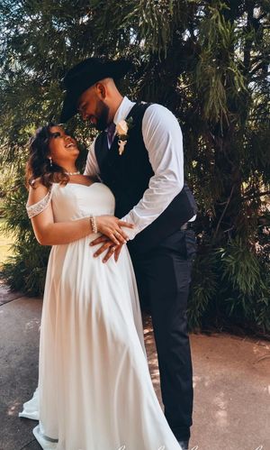 A romantic wedding couple embraces outdoors in a garden setting with lush greenery in the background.