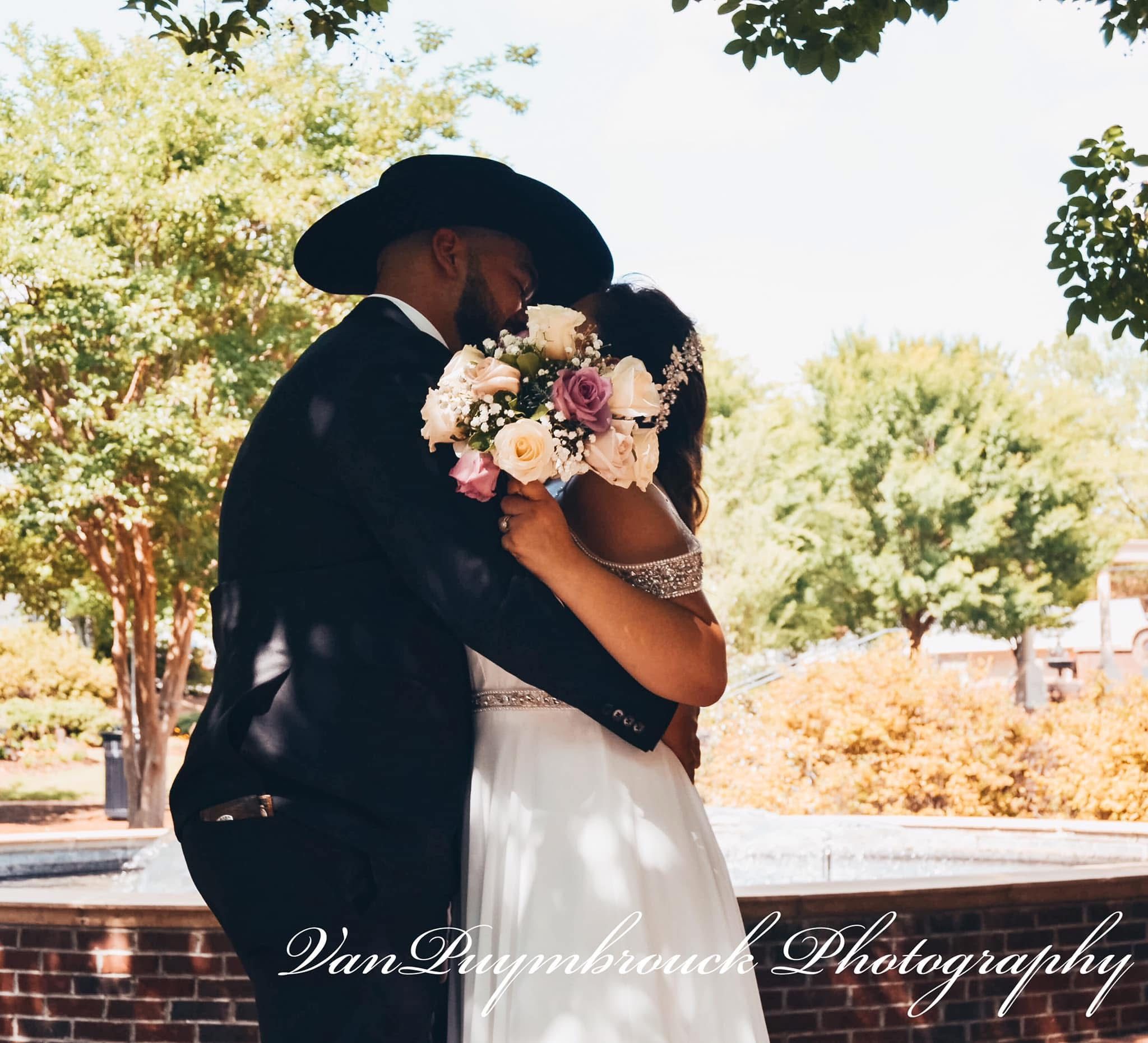 A romantic wedding portrait shows a couple in formal attire embracing against a garden backdrop with pink flowers.