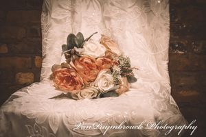 A detailed shot of a white wedding dress with ruffled fabric and delicate lace details against a dark background.