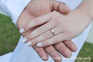 Close-up view of hands with engagement rings against a soft outdoor background.