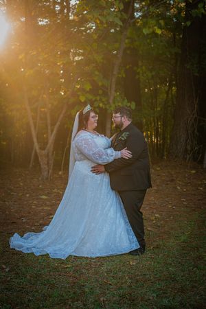 Couple shares intimate moment in forest clearing with warm sunset light glowing through trees.