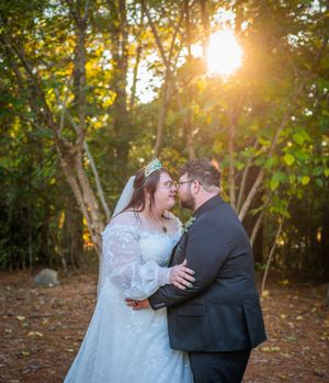 A romantic sunset wedding photo with golden light streaming through trees in a wooded setting.