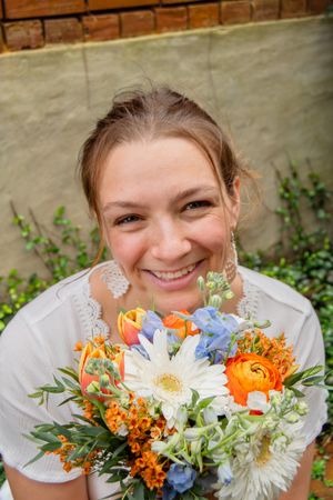 A bright and cheerful bouquet featuring orange ranunculus, white daisies, blue delphinium and greenery.
