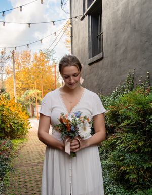 A white dress and autumn foliage create a romantic outdoor setting with string lights overhead.