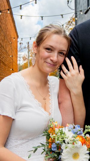 A white lace dress and colorful bouquet featuring daisies and orange flowers create a romantic autumn scene.