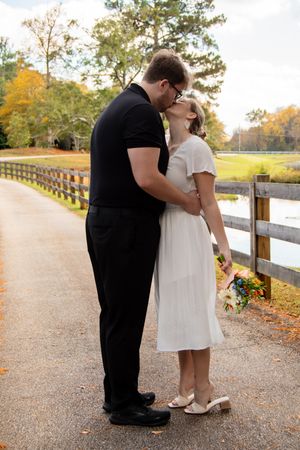 A couple shares an intimate moment on a gravel walkway bordered by wooden fencing during fall season.