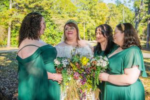 A group in emerald green dresses stands together in a sunny outdoor garden setting during a celebration.