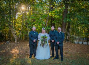 Wedding party poses in a wooded outdoor setting with golden sunlight filtering through autumn trees.