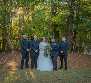Wedding party poses together in a wooded outdoor setting during golden hour with fall foliage in the background.