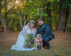 Wedding couple poses with their dog in a scenic autumn forest setting.