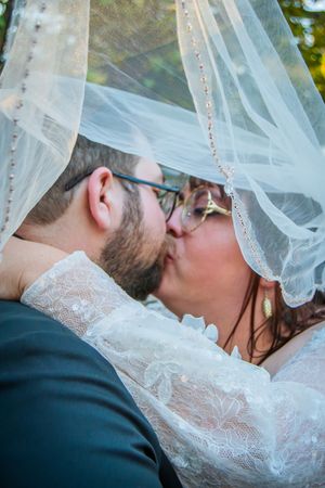 Close-up detail of romantic kiss under delicate lace veil during outdoor wedding ceremony.