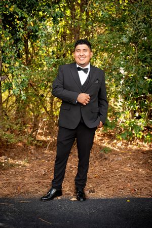 A formal event photo showing dress shoes and black suit pants against a natural outdoor backdrop.