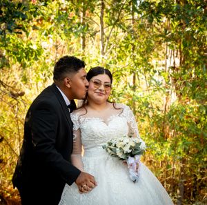 A romantic wedding moment captured in front of golden autumn foliage with a beautiful white lace ball gown and bouquet.