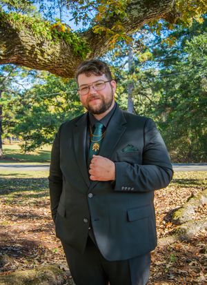 Groomsmen in dark suits pose casually against a sunlit autumn backdrop with trees and fallen leaves.