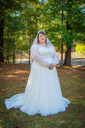 Bride in white lace wedding dress poses gracefully on grass in an outdoor autumn setting.