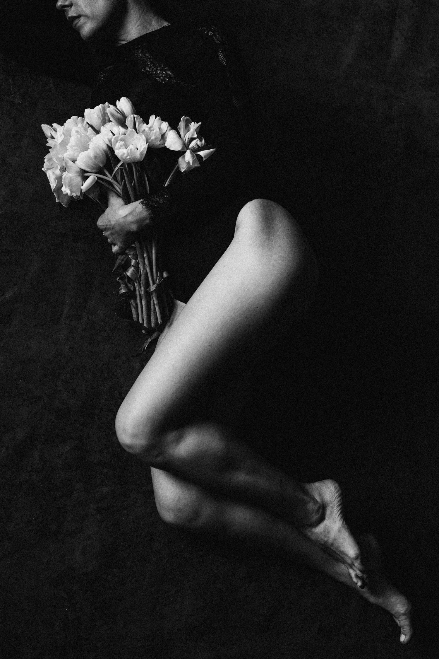Black and white artistic photo of a woman in a black bodysuit holding a bouquet of white tulips.