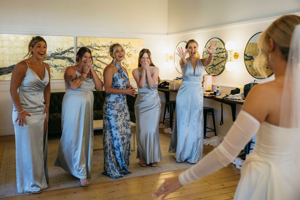 A group of people in light blue and floral dresses dance in a line at an indoor venue.