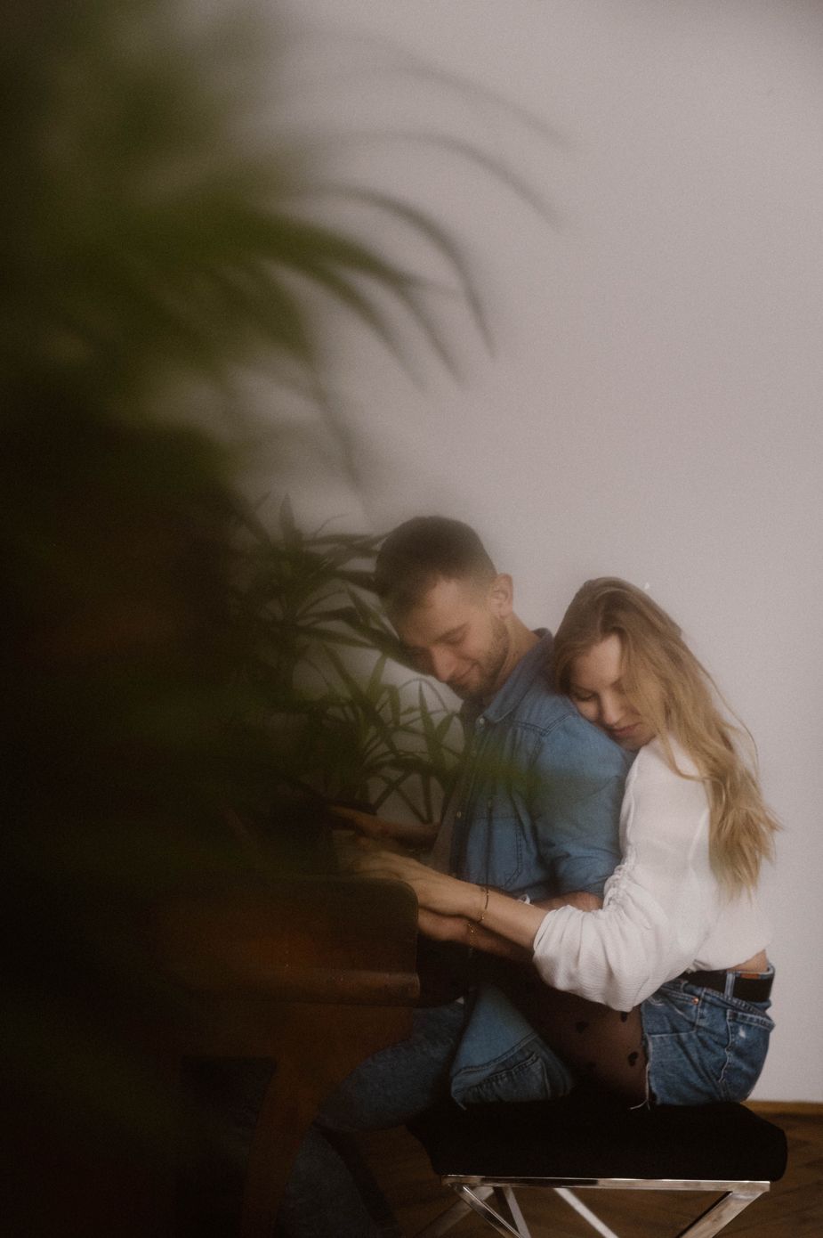 A romantic couple in moody lighting embraces intimately while sitting together in a dark setting.
