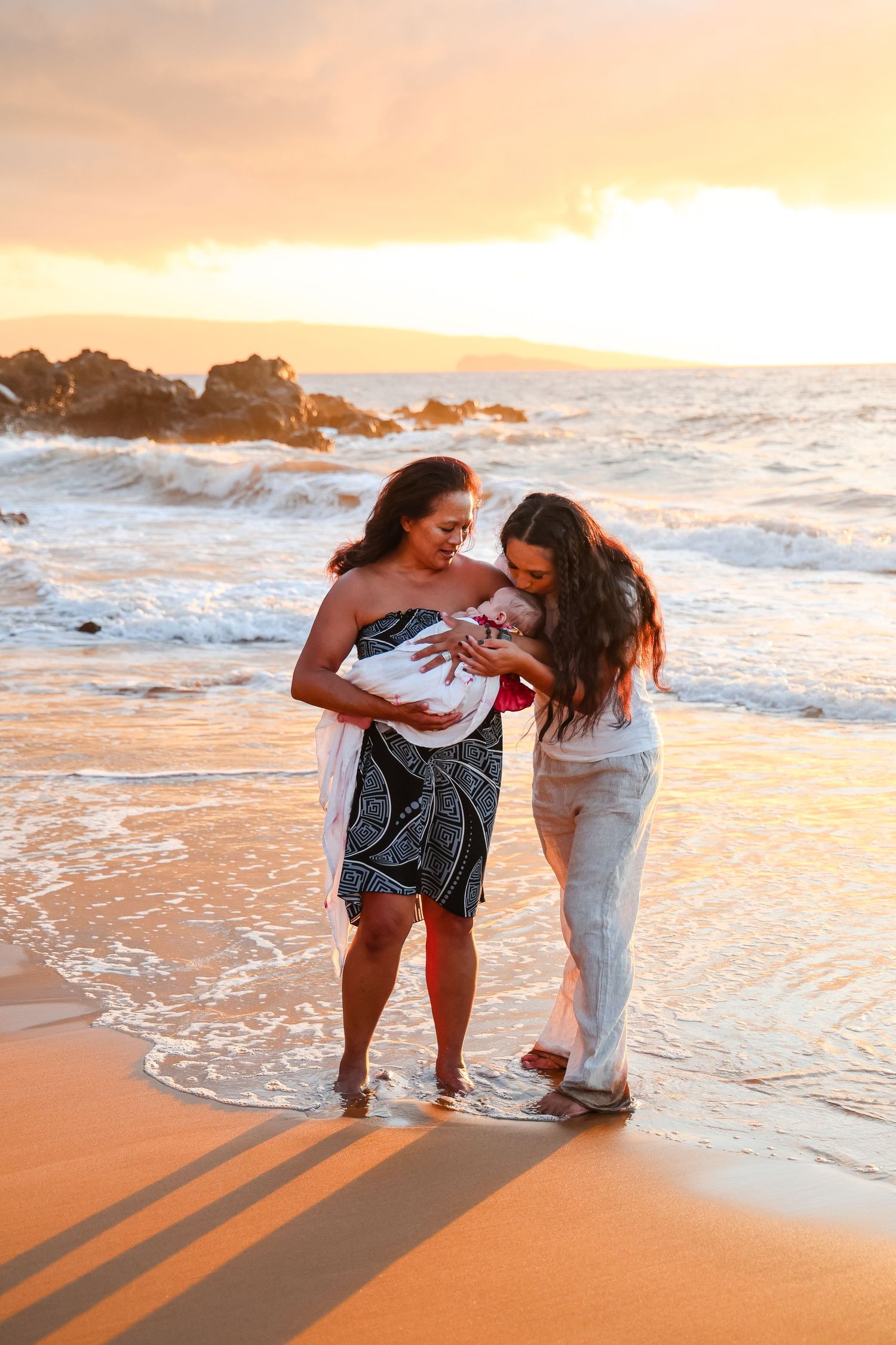 Two people stand in the ocean waves at sunset, sharing a tender moment on the beach.