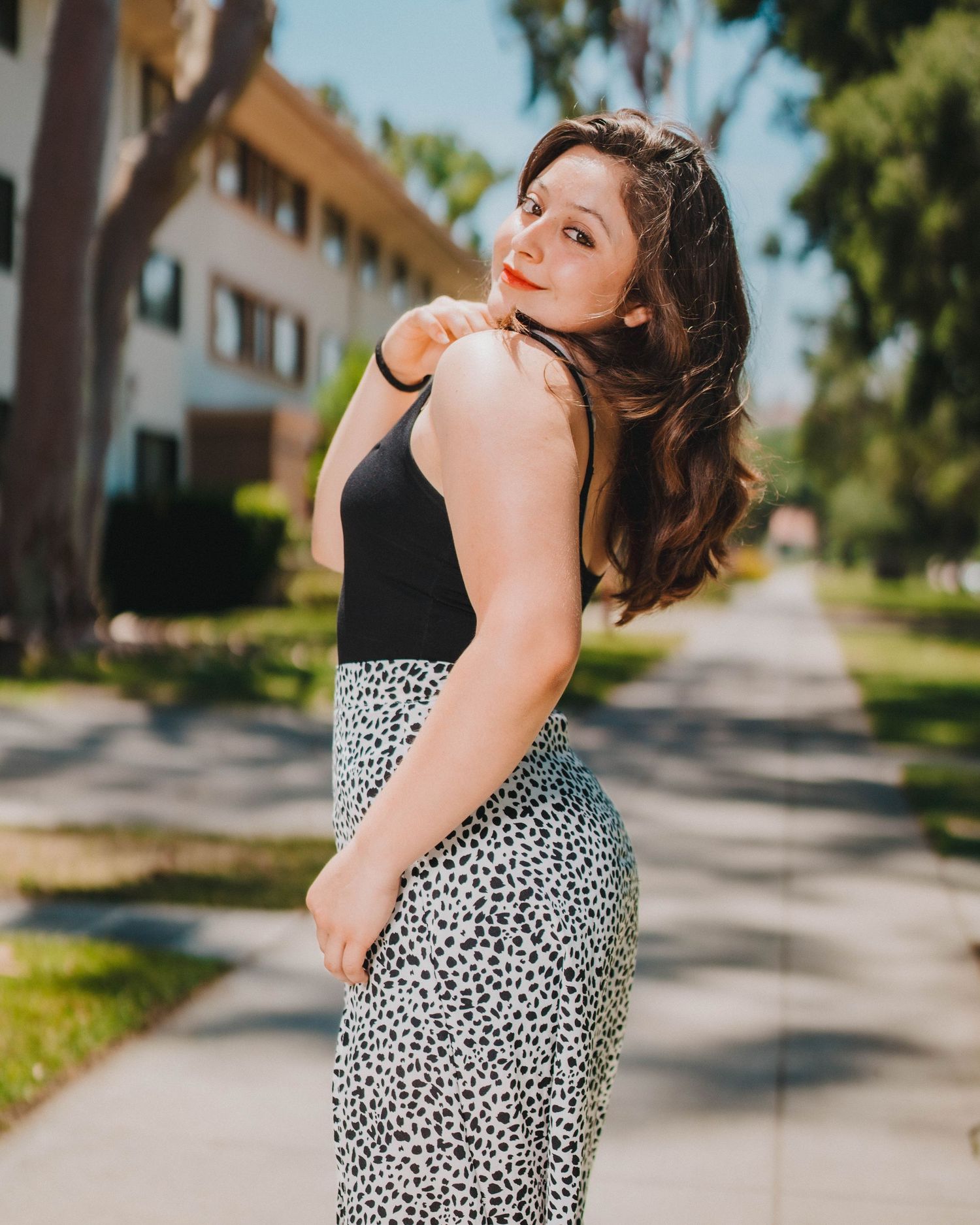 A person in a polka dot dress poses playfully in a series of shots on a tree-lined suburban street.