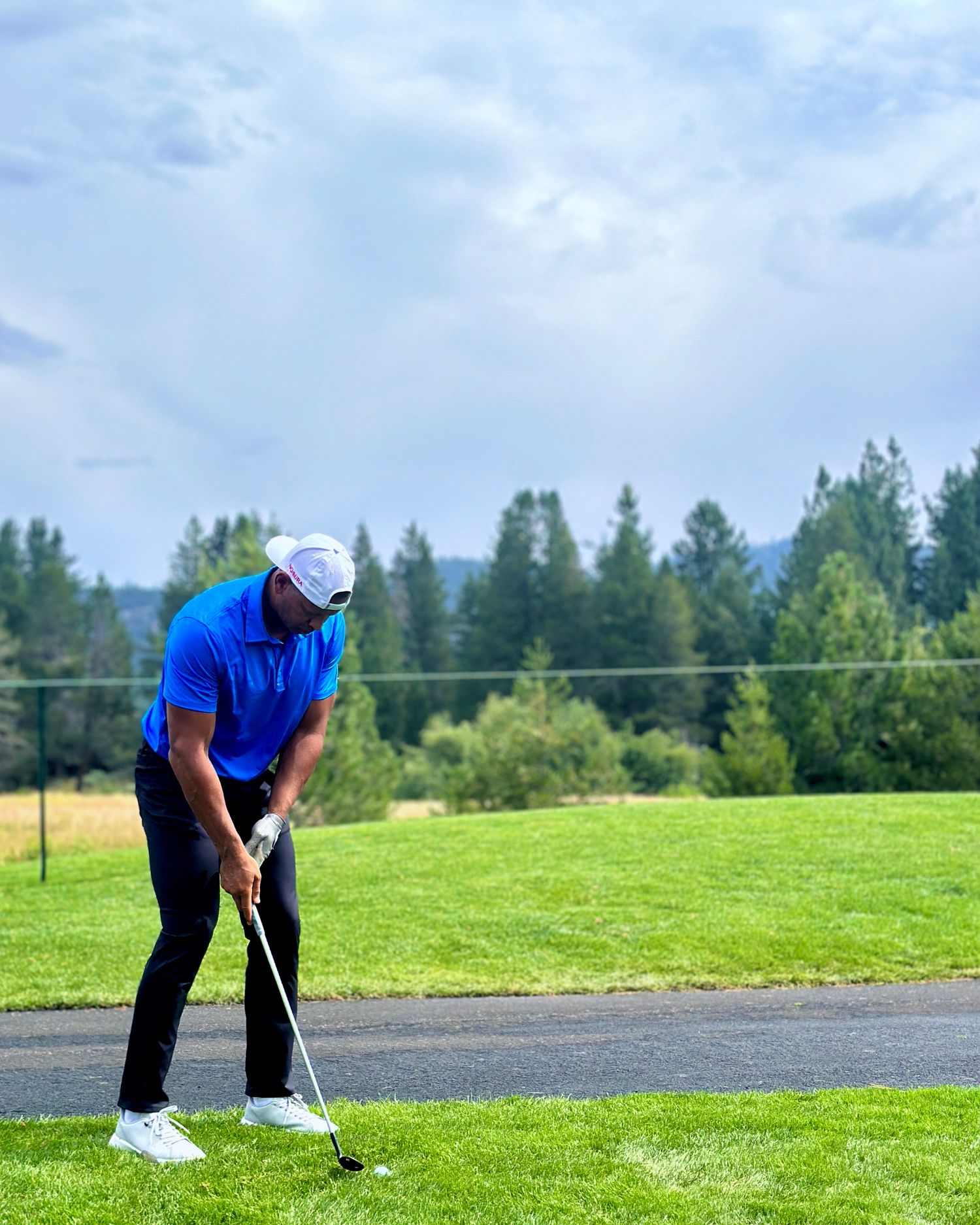 Golfer practicing their putting technique on a green course with forest backdrop.