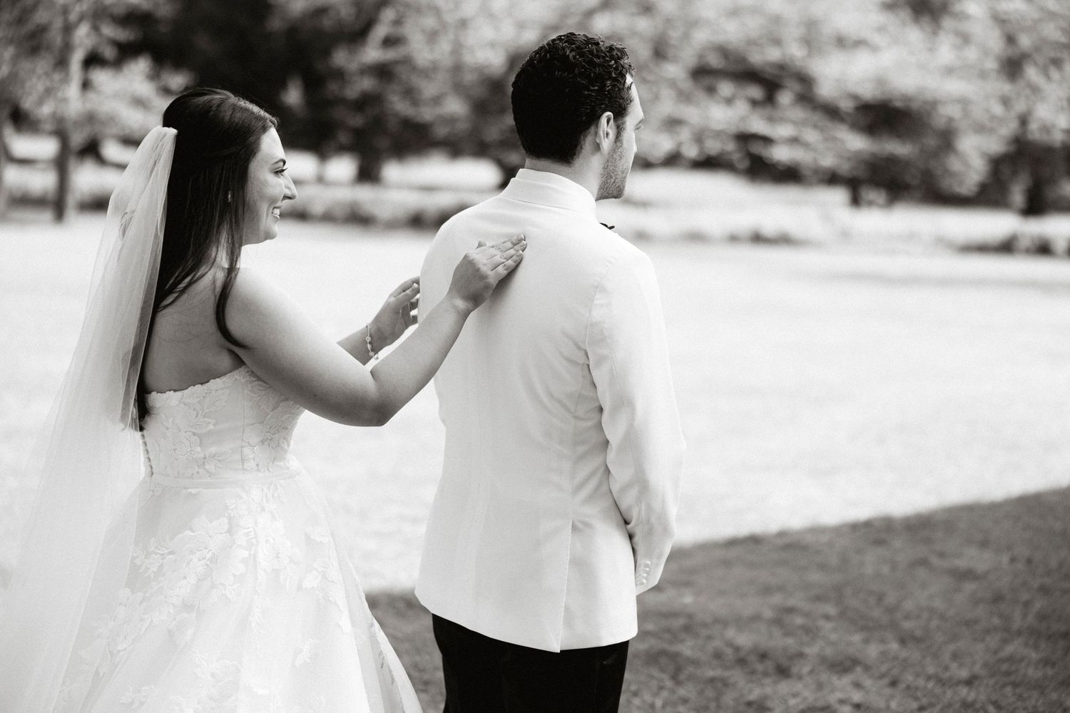 A couple in wedding attire dance together outdoors in black and white photography.