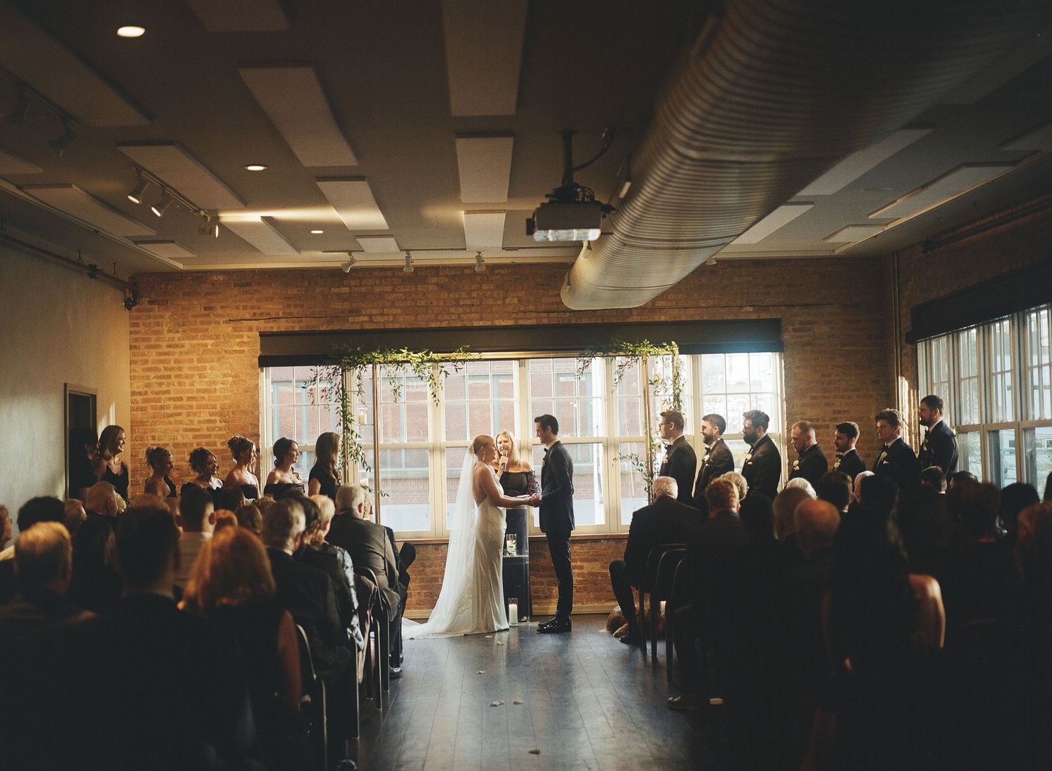 Wedding ceremony in an industrial brick venue with guests seated around the couple.