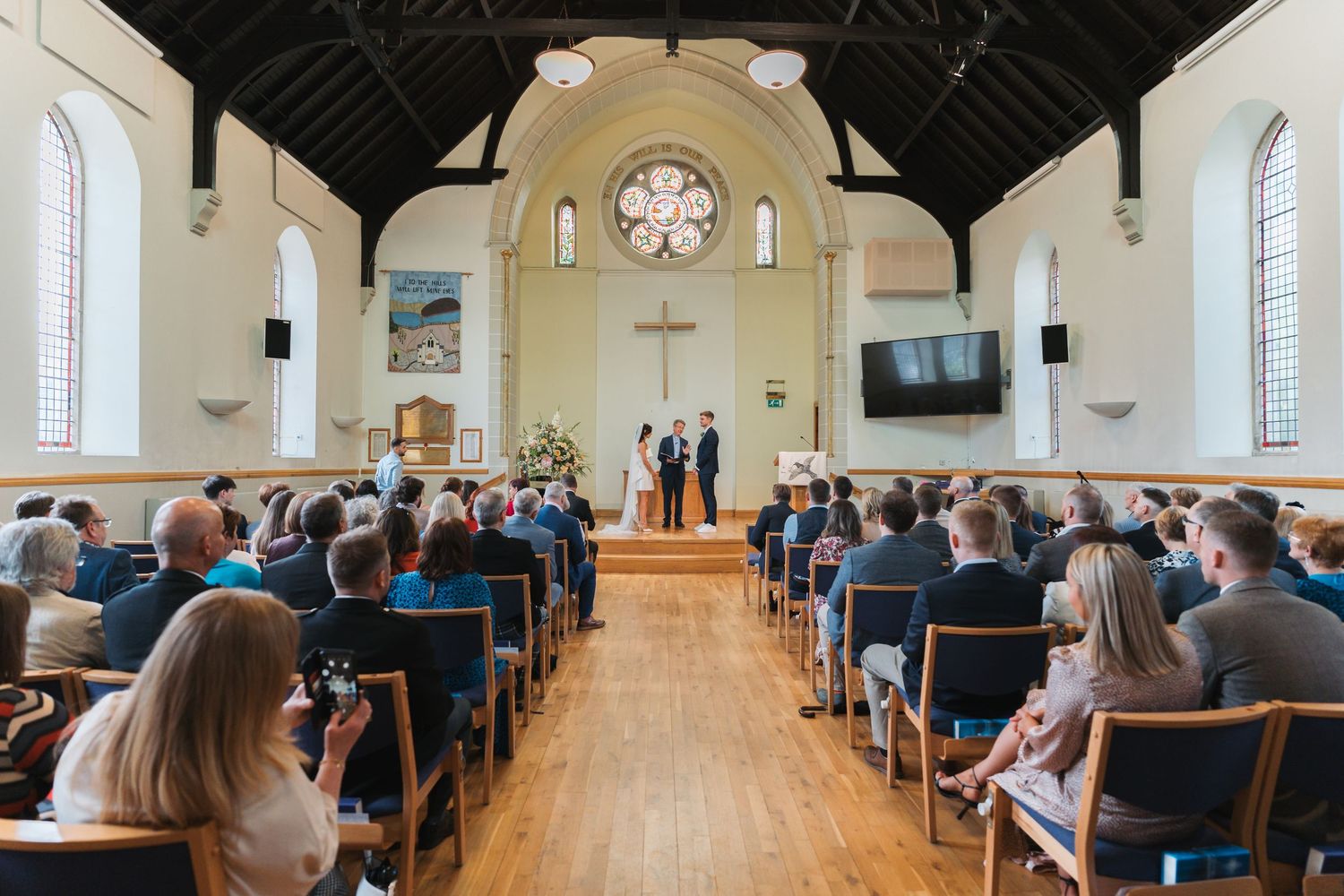 Panoramic view of a traditional church interior during a wedding ceremony with guests seated in wooden pews.