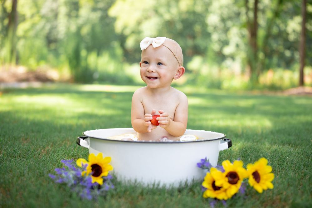 Sunflowers surround a white antique wash basin in a sunny outdoor garden setting.