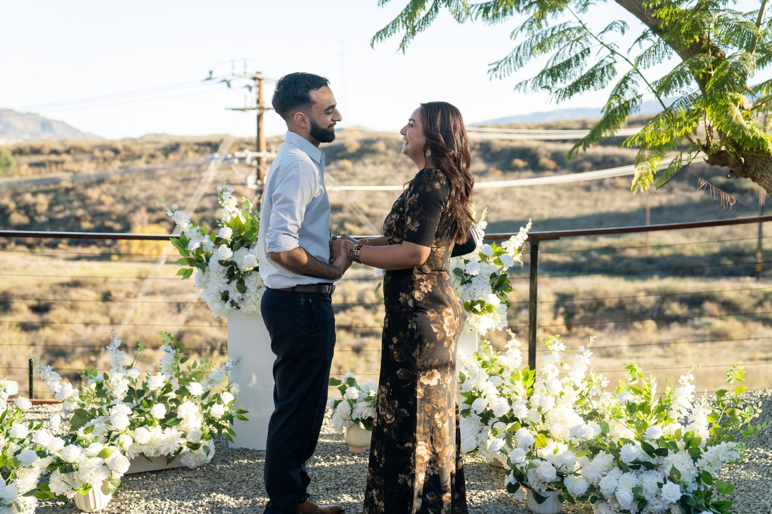 A romantic couple shares tender moments in a desert landscape surrounded by blooming white flowers and mountains.