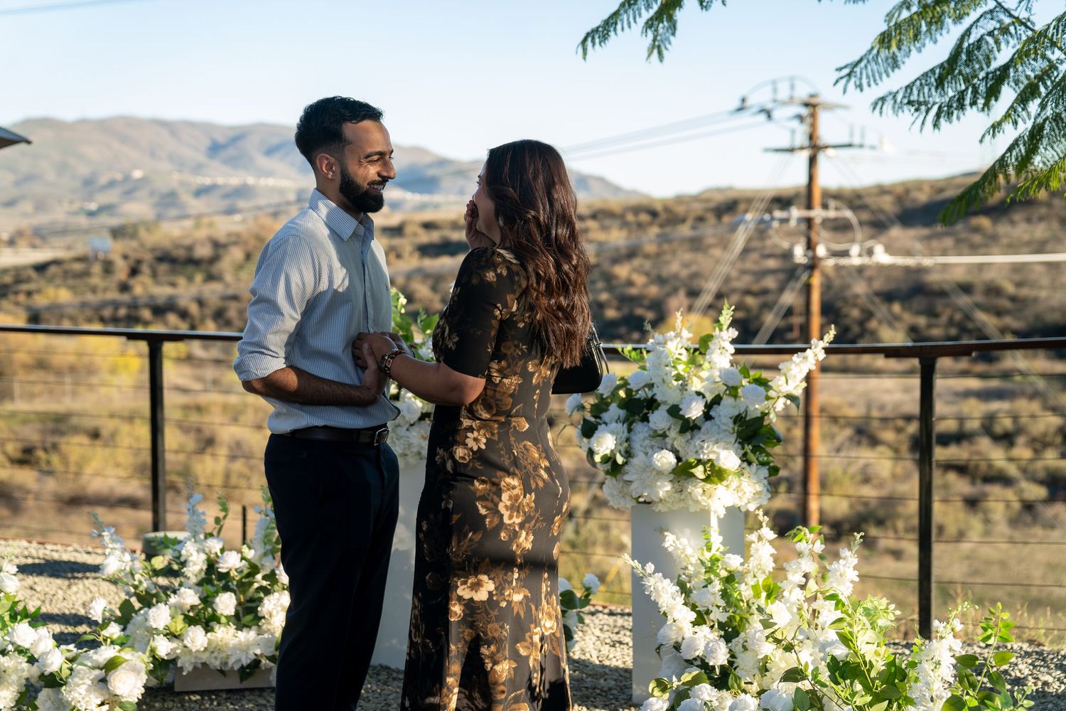 A couple shares an intimate moment at a rustic outdoor ceremony decorated with white floral arrangements in a desert setting.