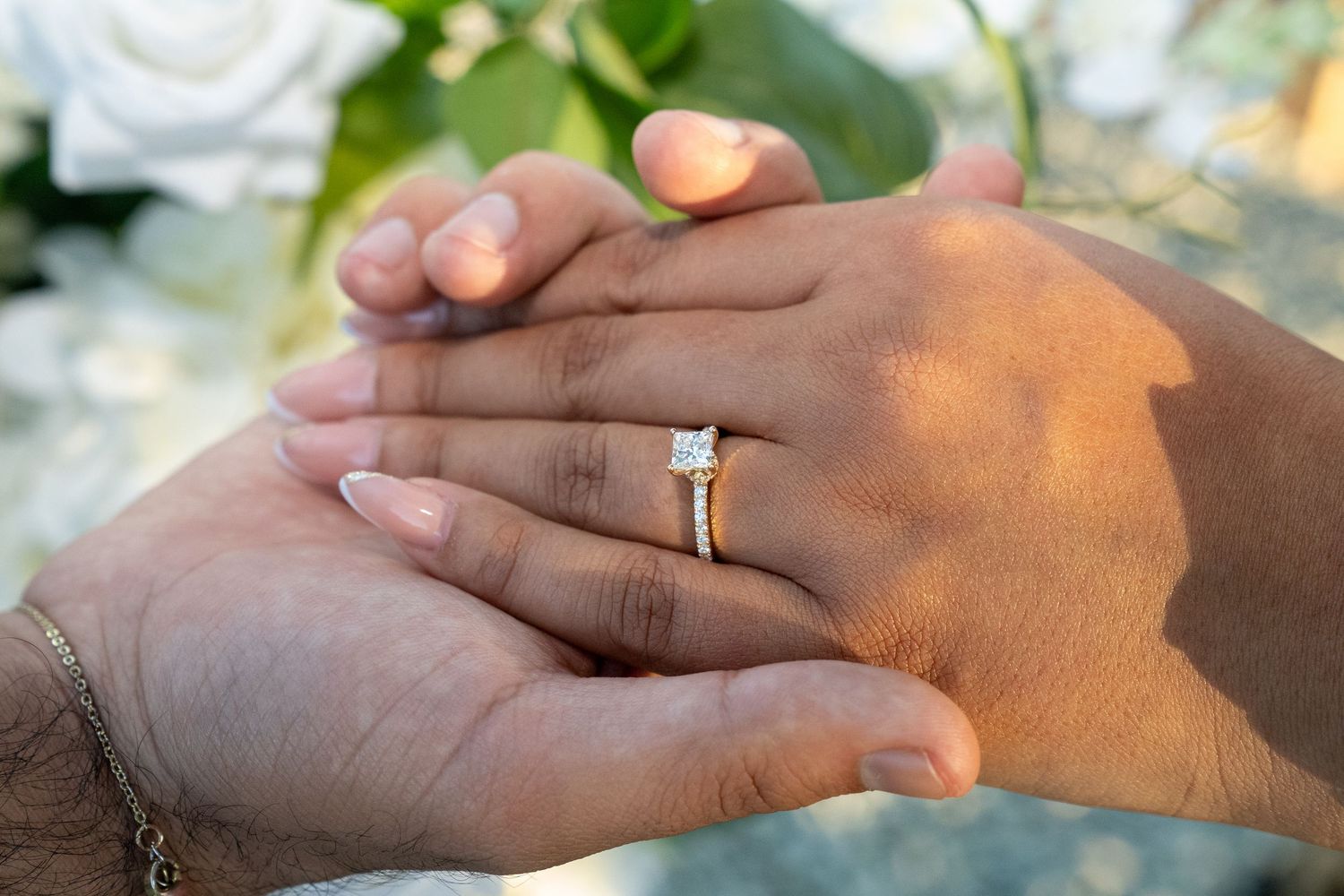 Close-up shot of hands holding each other with an engagement ring in warm sunlight.