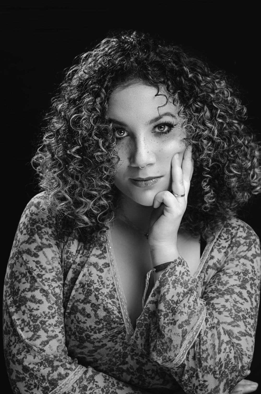 Retrato artístico em preto e branco com foco em cabelos cacheados. Ensaio feminino com iluminação dramática em estúdio.