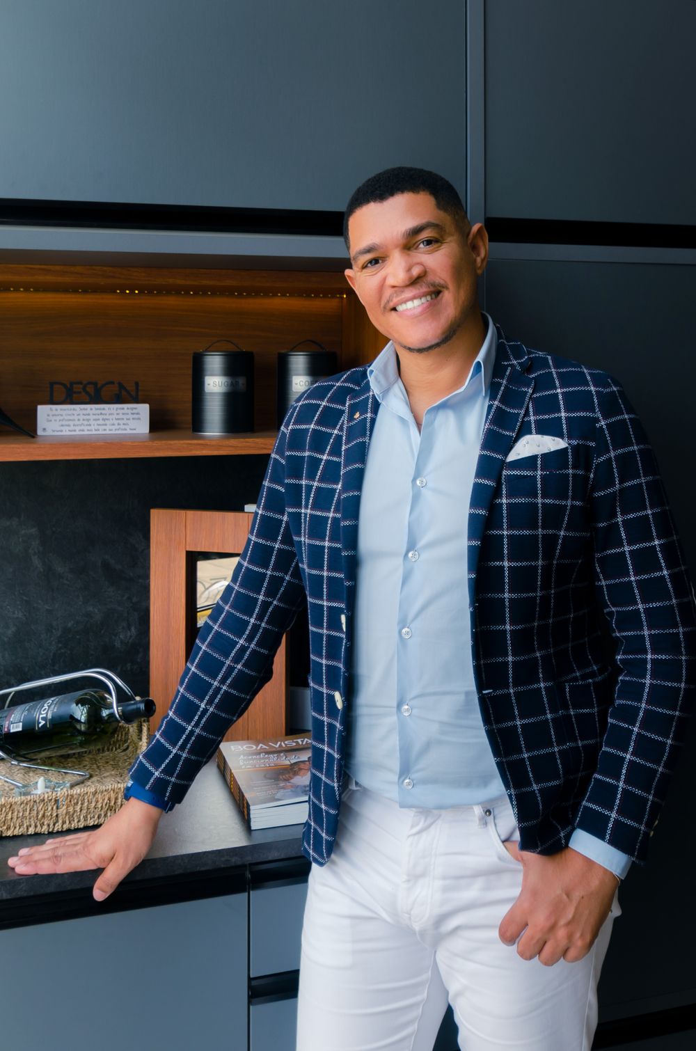Retrato corporativo moderno de empresário sorrindo com blazer xadrez, em frente a uma estante. Exemplo de headshot executivo.