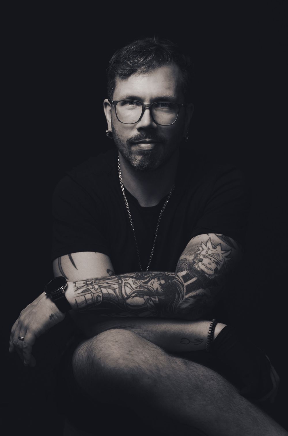 Retrato masculino em estúdio na Tijuca. Homem sentado com braços cruzados, luz dramática e fundo escuro. Fotografia profissional masculina.