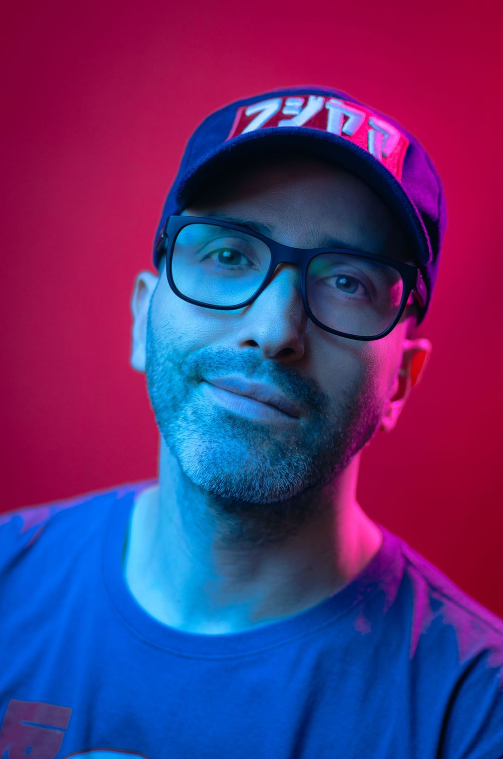 Retrato criativo masculino com luzes neon azul e rosa. Homem de boné e óculos, exemplo de fotografia artística para perfis modernos.