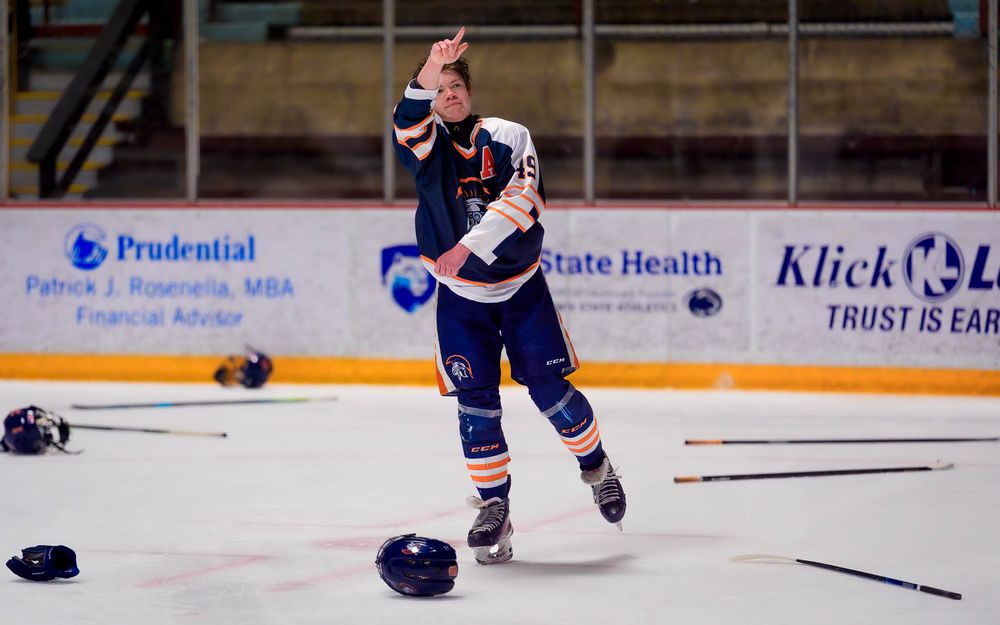Trojans player skates across the ice, celebrating with stick raised and gear scattered after the championship win by SportsFox Photography,