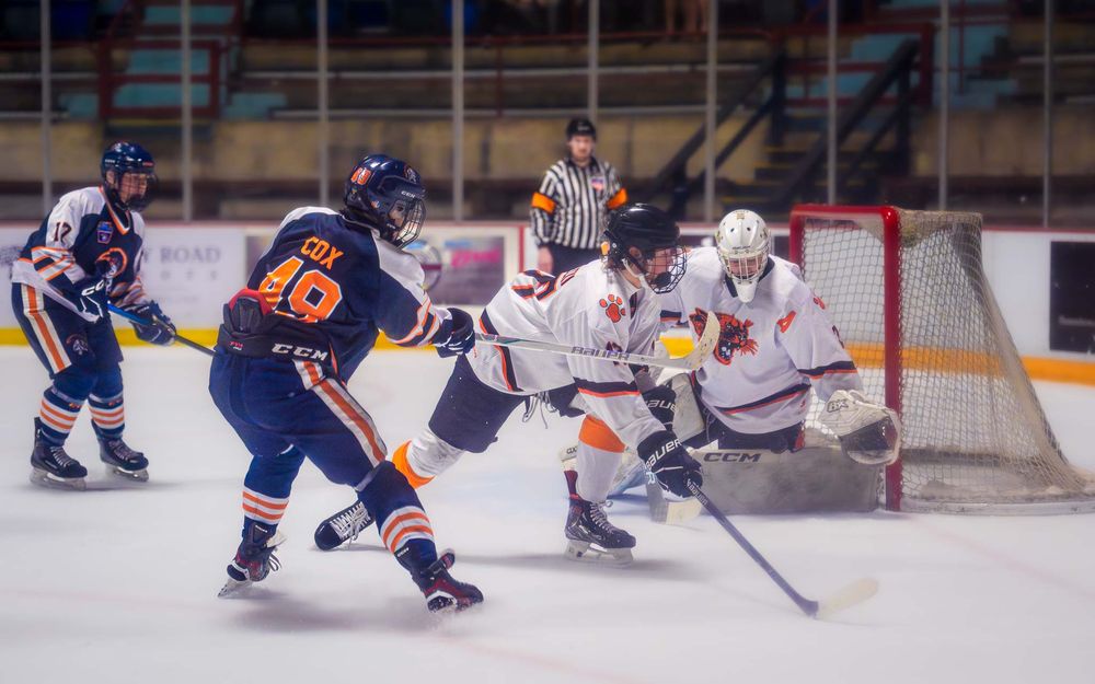 Trojans player fires a shot on goal, with the puck heading toward the net by SportsFox Photography, Hershey PA.
