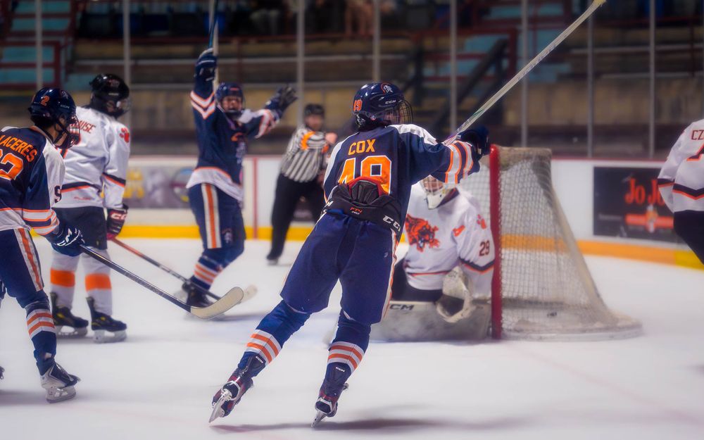 Trojans player fires a shot on goal, with the puck heading toward the net by SportsFox Photography, Hershey PA.