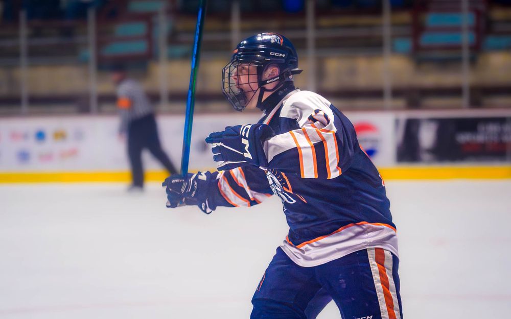 Trojans player skates with stick raised, celebrating a big moment on the ice by SportsFox Photography, Hershey PA.
